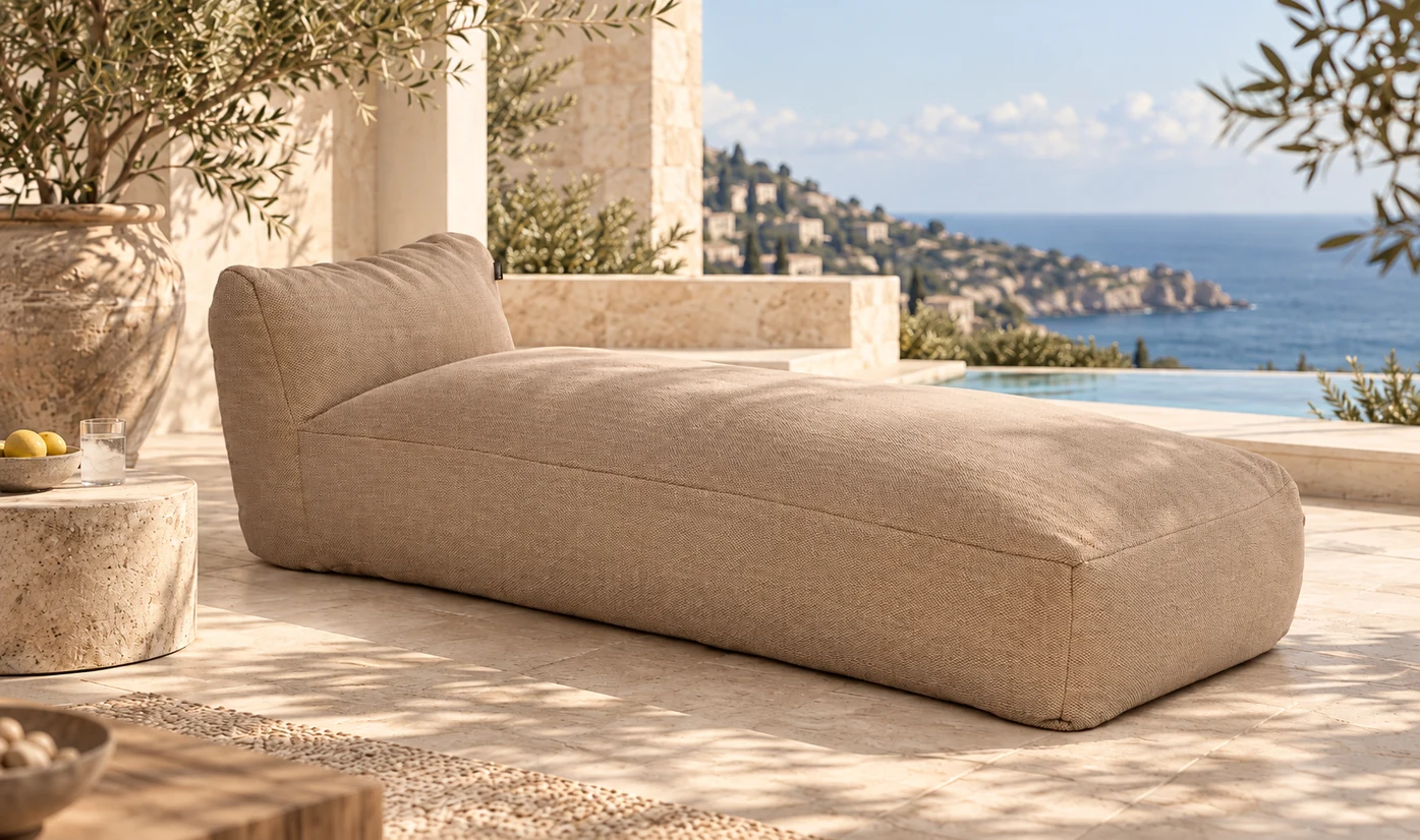Beige upholstered outdoor sun lounger on a stone terrace overlooking the sea